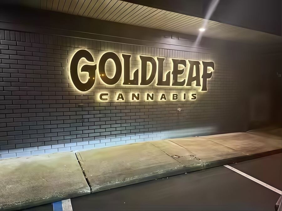 Goldleaf Cannabis gold backlit channel letters on dark brick wall at night